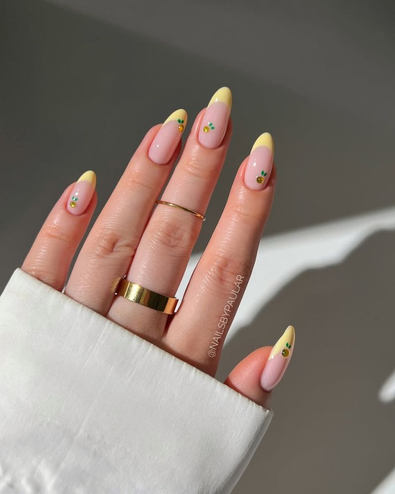 butter yellow french tips with tiny orange citrus and green leaf details on almond nails
