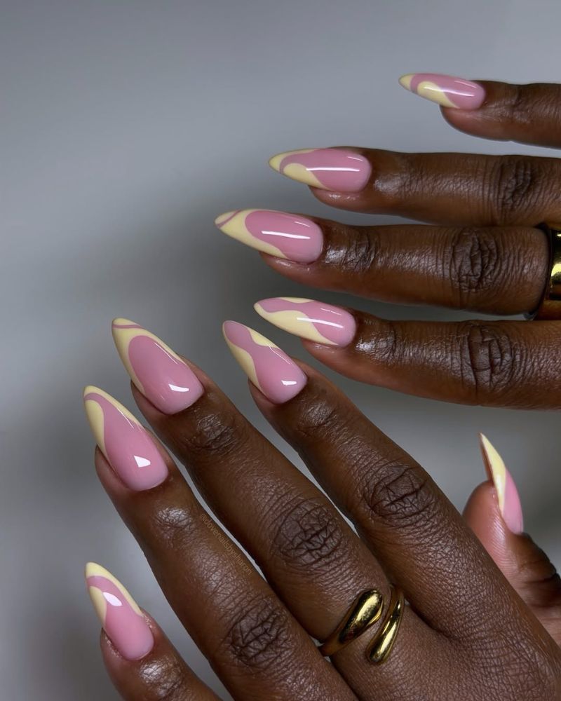 pink and butter yellow color-block french tip nails divided by a wave curve on long almond nails