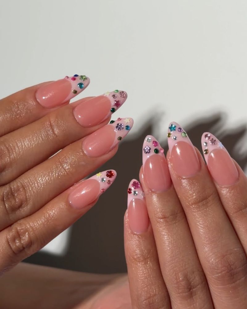 warm pink french tip nails covered in multicolor rhinestone gems in the tip area on almond nails