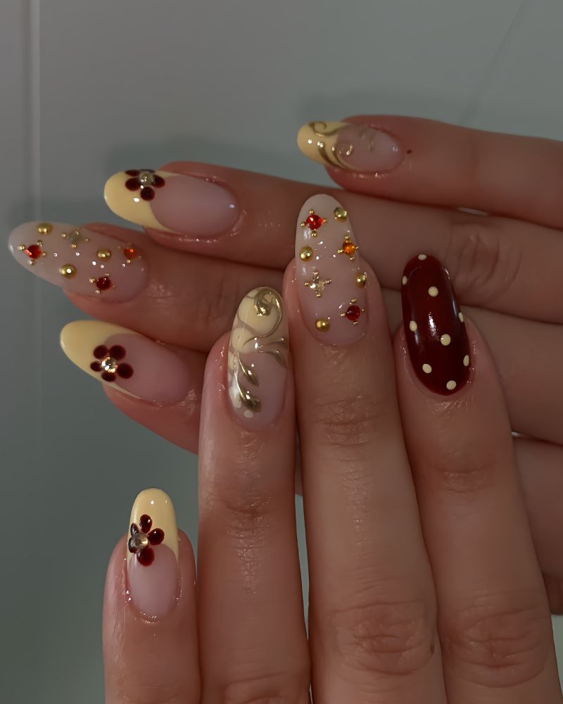 butter yellow french tips with dark cranberry flowers and gem accents