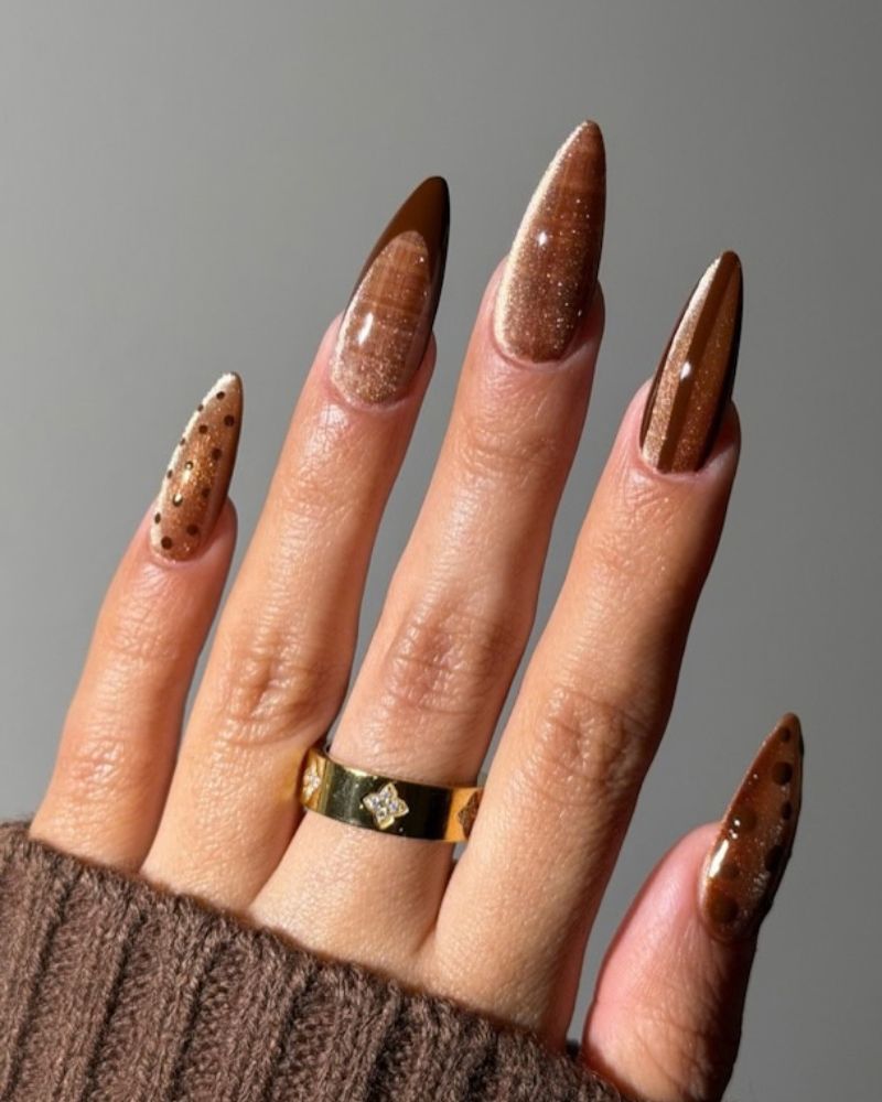 long almond chocolate brown nails with dense copper shimmer and small dark dot accents on two nails gold clover ring brown knit sweater