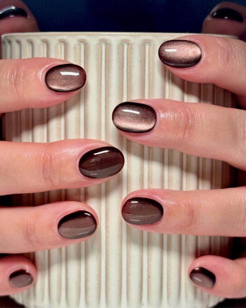 short oval dark brown nails with rose bronze cat eye shimmer both hands wrapped around white ribbed ceramic cup navy background