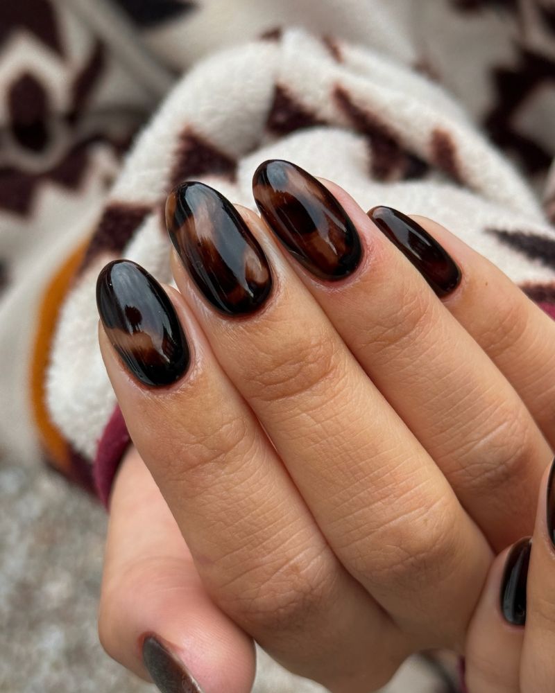 medium almond near black tortoiseshell nails dark brown with warm amber swirling through high gloss cozy patterned fabric background