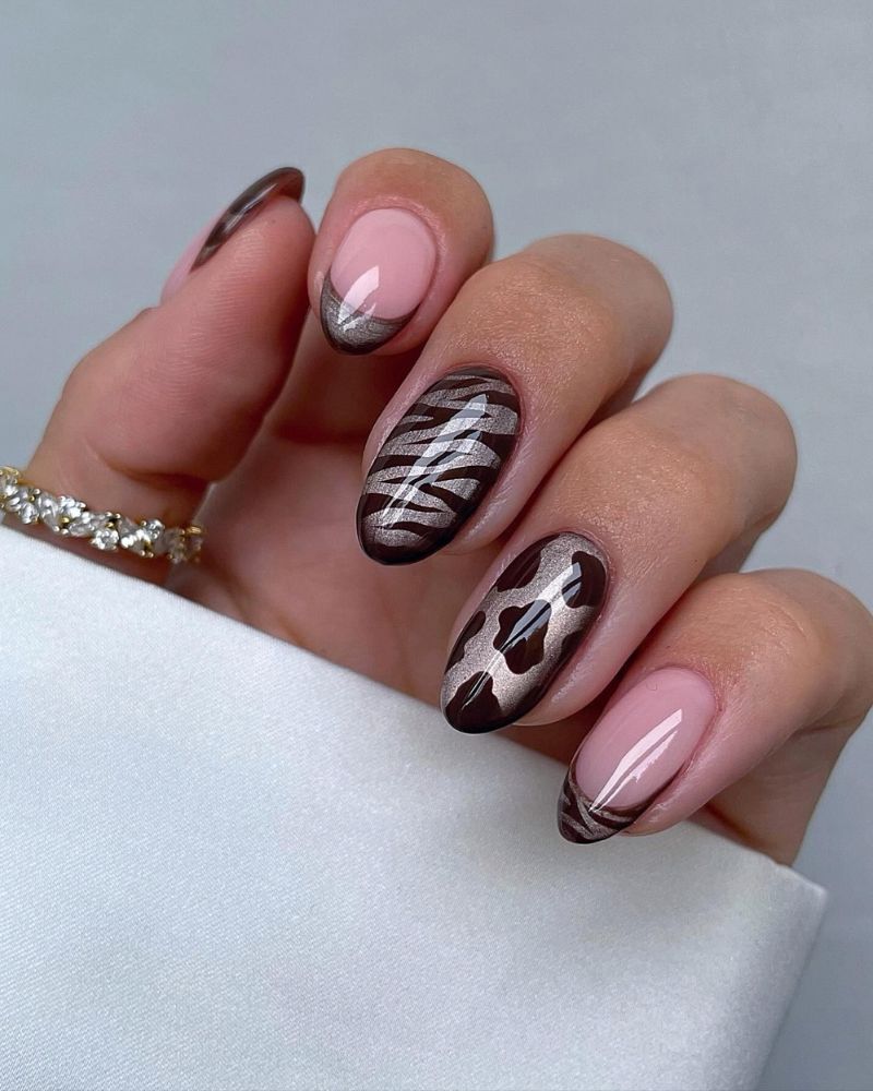 short almond nails taupe shimmer base mixed set dark chocolate zebra stripes on some nails cow spots on others and plain nude nail white crystal eternity bracelet white surface