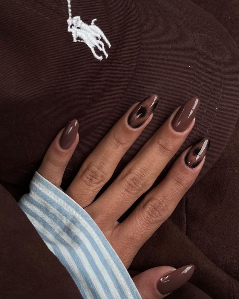 medium long almond nails in warm mid-tone chocolate brown very glossy against dark brown ralph lauren hat blue striped sleeve