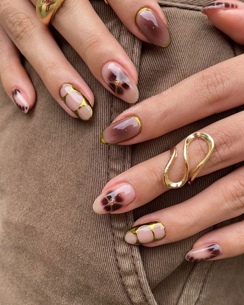 short medium almond nails mixed set nude nails with thin gold rectangular outline frames and dark brown ink blooms inside frames sculptural gold s ring khaki pants