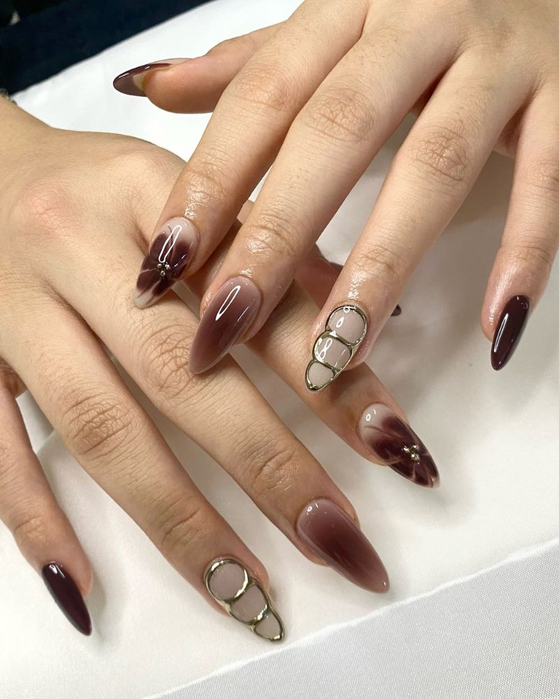 long almond nails dark wine brown solid alternating with nude nails with brown aura smoke and 3d gold bubble chain charms embedded in gel two hands