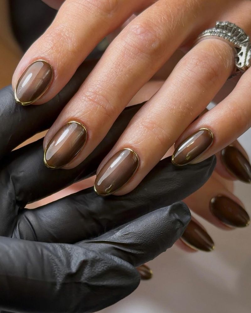 short oval chocolate brown nails with fine gold outline frame around each nail black leather glove backdrop silver crystal ring